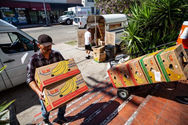 A man carrying boxes of bananas down a street.