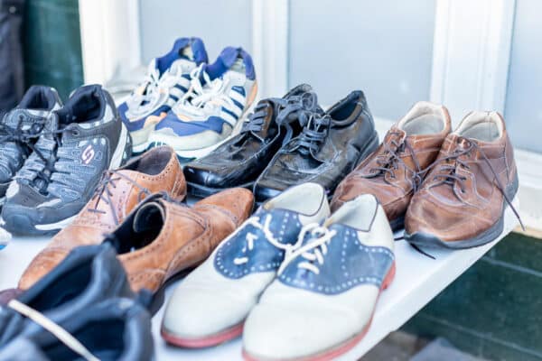 Many pairs of shoes on a table in front of a window.