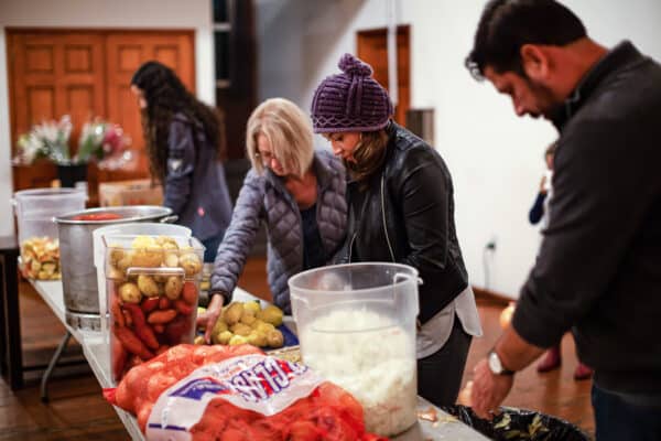 A group of people standing around a table full of food.