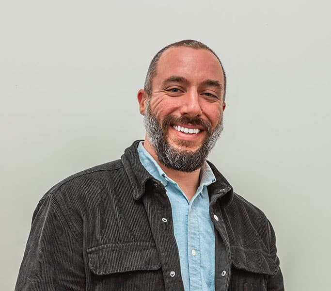 A man with a beard smiling in front of a white background.