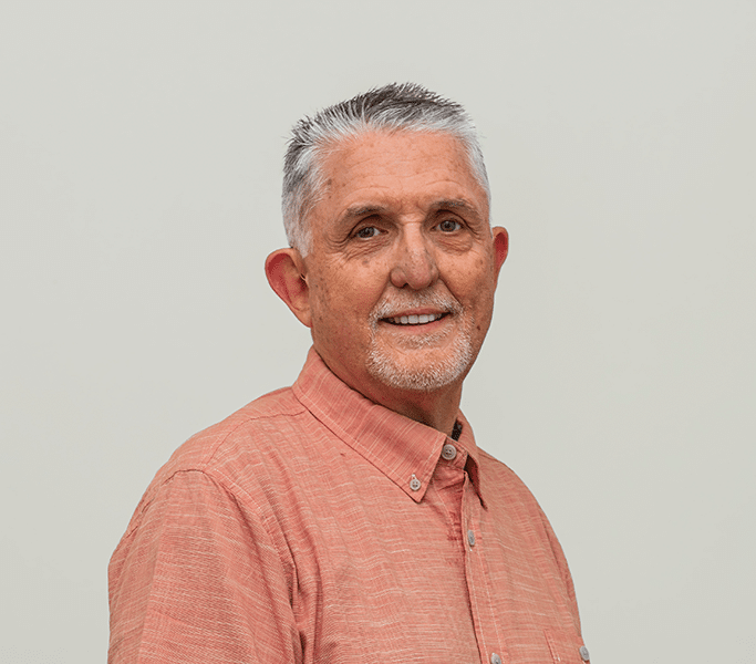 A man in an orange shirt standing in front of a white background.